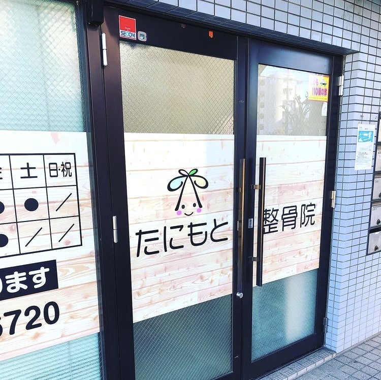 たにもと整骨院の入口。すりガラスの自動ドアに院名ロゴと診療時間表が掲示されている