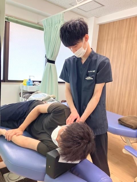 たにもと整骨院の施術者が、横向きに寝た患者の首から肩にかけてをていねいに施術している様子